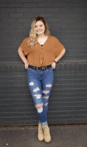 A woman smiles while standing in front of a black brick wall. 